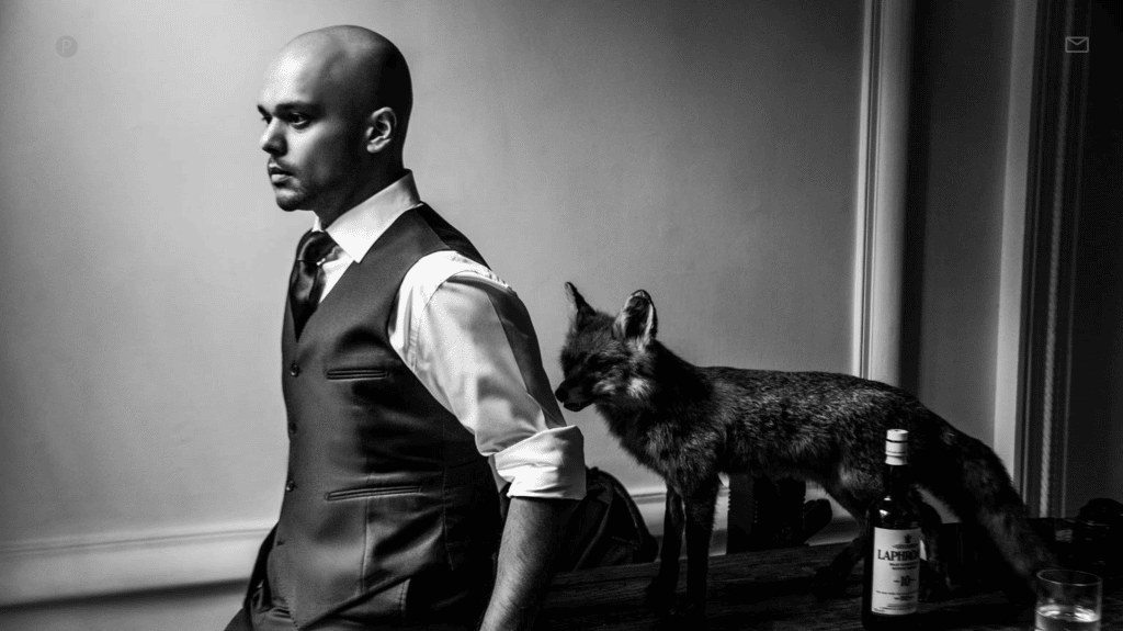 Male standing wearing a suit with dog behind him.
